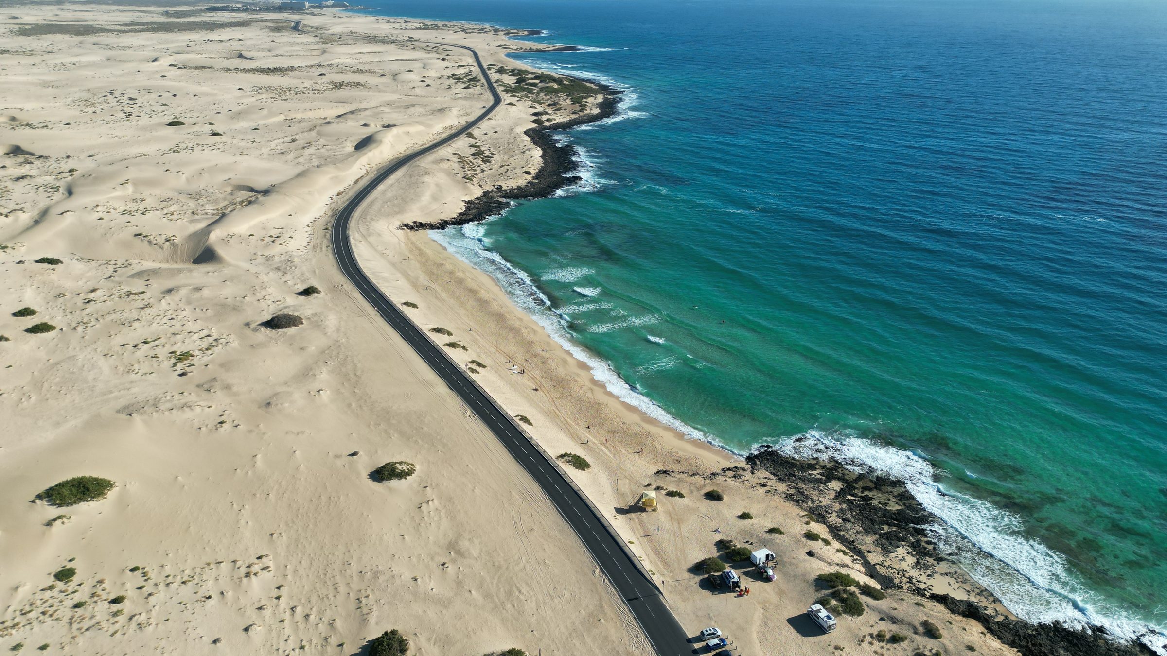 Route côtière serpentant entre dunes dorées et océan turquoise à Fuerteventura